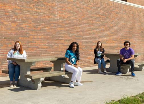 Four student leaders sit at concrete picnic tables outside
